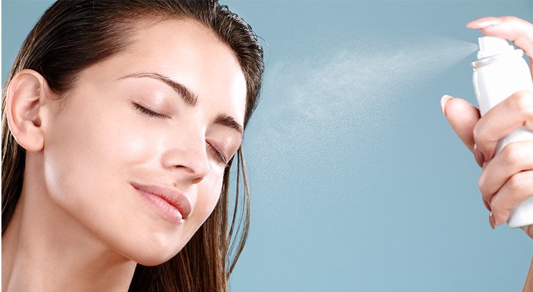 Eine Frau sprüht ein Gesichtsspray auf