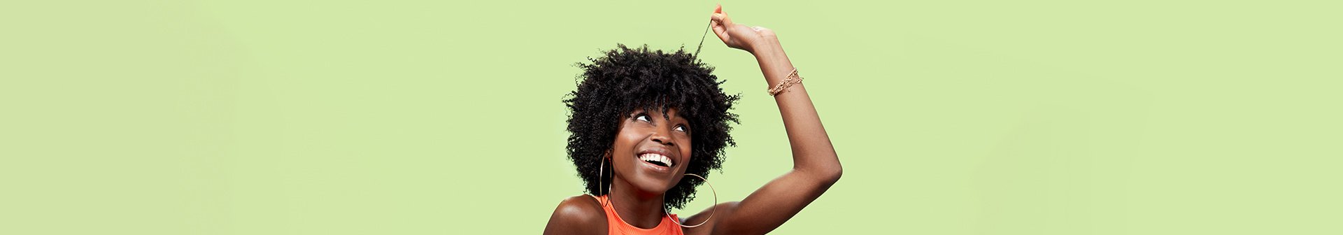 Junge Frau mit lockigen Haaren  betrachtet lächelnd eine Strähne ihres Haares