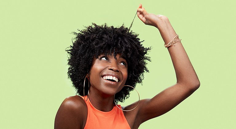 Junge Frau mit lockigen Haaren  betrachtet lächelnd eine Strähne ihres Haares