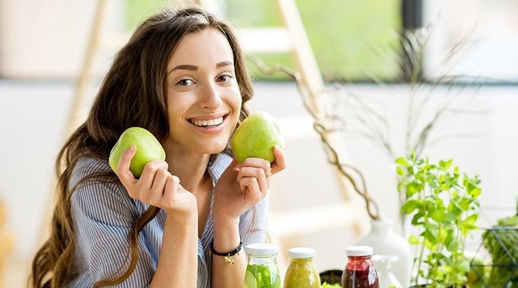 Frau hält Äpfel neben ihr Gesicht