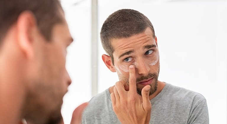 Mann trägt Creme auf die Augenpartie auf