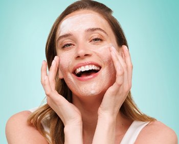 Lachende Frau reinigt ihr Gesicht mit einem Cleanser