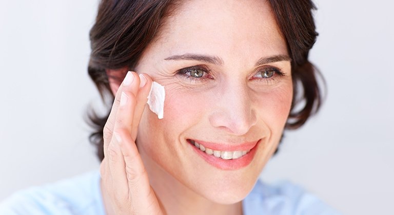 Eine Frau trägt Creme auf ihre rechte Wange auf