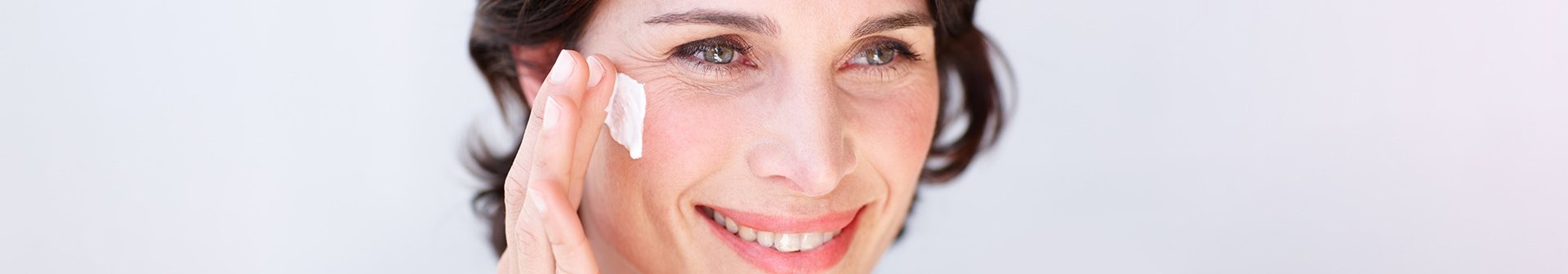 Eine Frau trägt Creme auf ihre rechte Wange auf