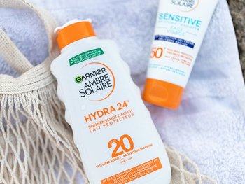 Handtuch im Sand auf dem zwei Sonnenschutzprodukte von Garnier Ambre Solaire liegen