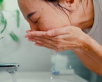 Junge Frau wäscht ihr Gesicht mit Wasser