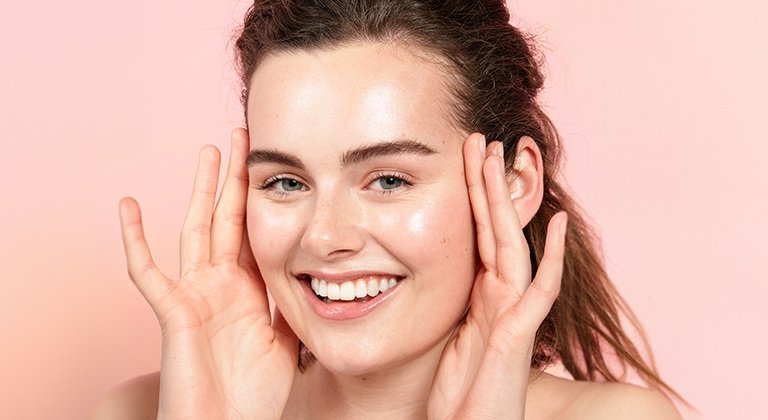 Eine lächelnde junge Frau mit Creme auf ihren Wangen & ihrer Stirn