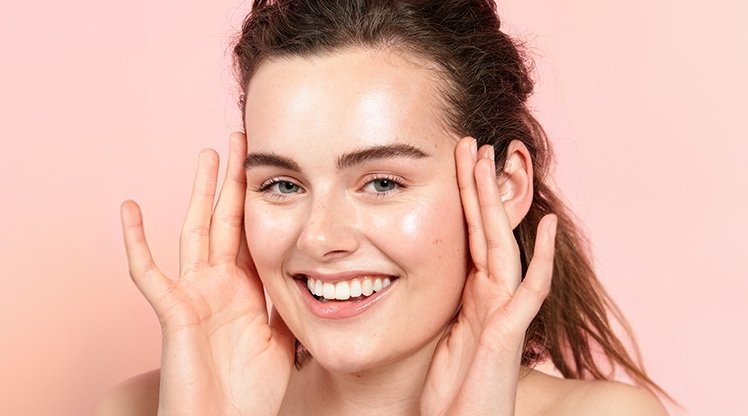 Eine lächelnde junge Frau mit Creme auf ihren Wangen & ihrer Stirn