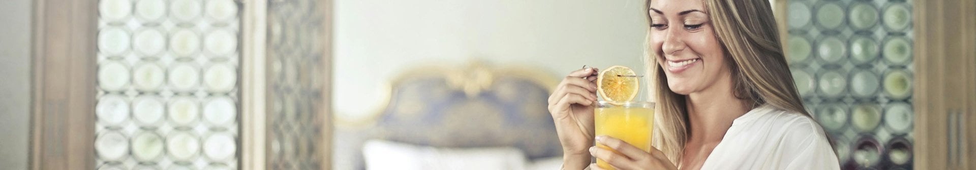 Bild einer blonden Frau, die ein Glas Orangensaft und eine Orangenscheibe hält