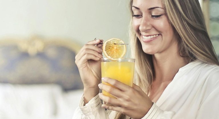 Bild einer blonden Frau, die ein Glas Orangensaft und eine Orangenscheibe hält