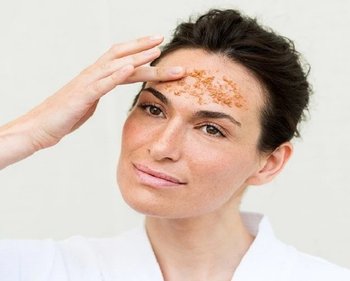 Frau trägt Peeling gegen fettige Haut auf der Stirn auf