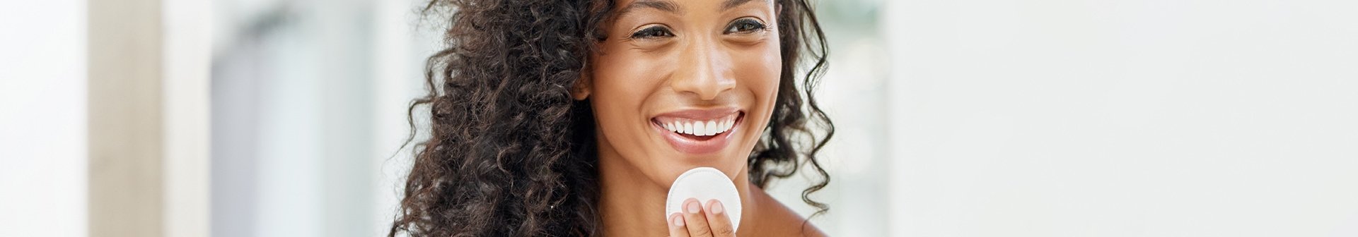 Junge Frau mit dunklen lockigen Haaren reinigt ihr Gesicht mit einem Pad
