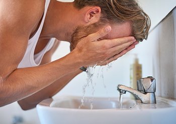 Mann mit blonden Haaren spült sich das Gesicht mit Wasser ab