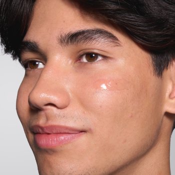 Nahaufnahme vom Gesicht eines jungen Mannes, Gesichtspflegeprodukt ist auf der Wange aufgetragen