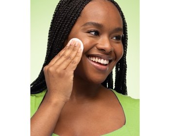 Junge lächelnde Frau reinigt ihre Haut mit einem Wattepad