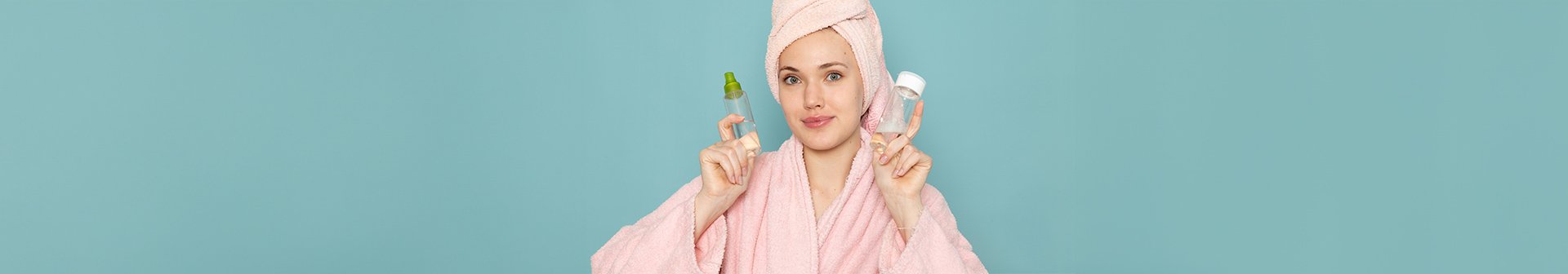 Ein junge Frau im Bademantel, die Haare in ein Handtuch gewickelt mit zwei kleinen Glasfläschchen in den Händen