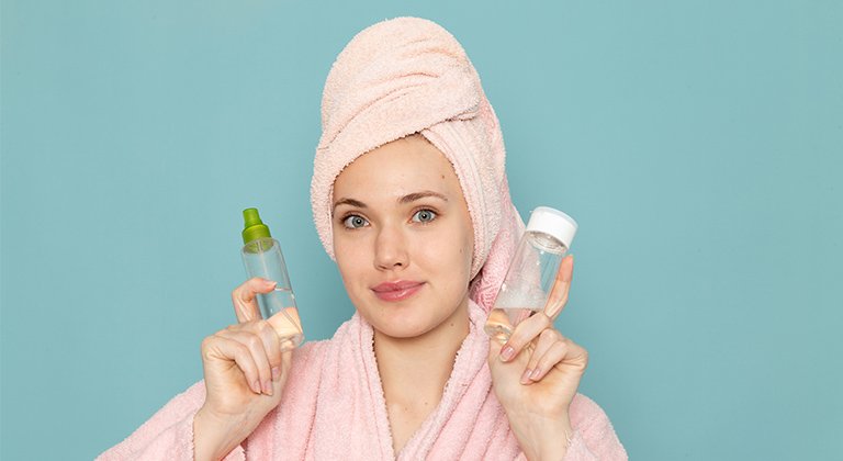 Ein junge Frau im Bademantel, die Haare in ein Handtuch gewickelt mit zwei kleinen Glasfläschchen in den Händen