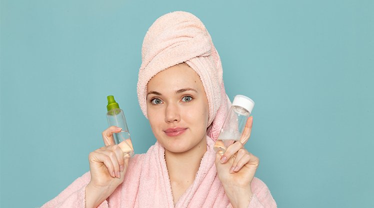Ein junge Frau im Bademantel, die Haare in ein Handtuch gewickelt mit zwei kleinen Glasfläschchen in den Händen