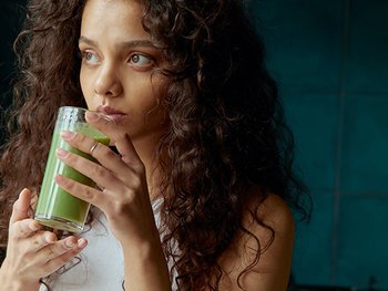 Lächelndes Gesicht einer Frau, die einen grünen Smoothie mit einem Strohhalm in der Hand hält