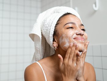 Gesicht einer Frau, die sich nach vorne beugt und mit Wasser in den Händen ihr Gesicht wäscht