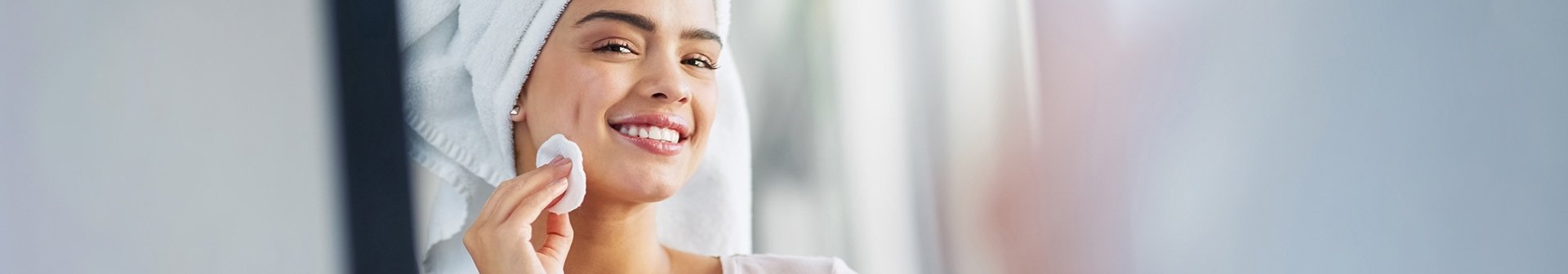 Lächelndes Gesicht einer Frau mit einem Wattepad in der Hand und einem Handtuch auf dem Kopf