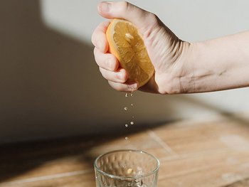 Hand drückt eine Zitronenhälfte aus, Saft tropft in ein Glas.
