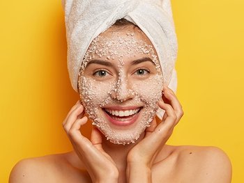 Frau mit einer peelenden Gesichtsmaske vor einer gelben Wand