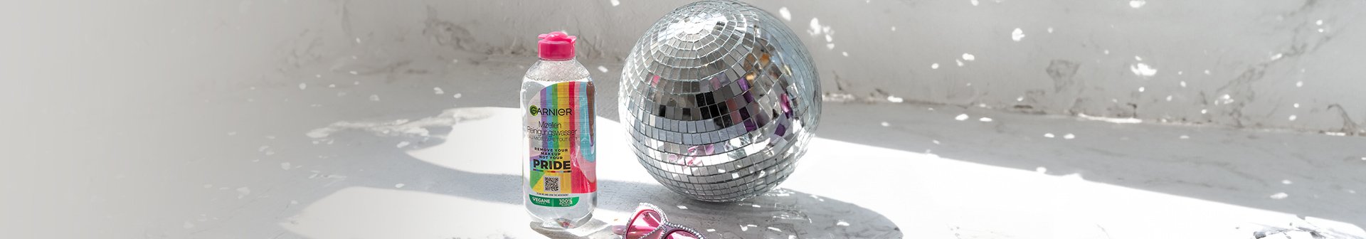 Mizellenwasser Pride Edition steht neben einer Discokugel und einer rosa Sonnenbrille