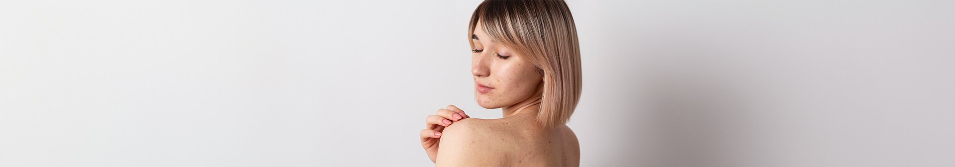 Eine junge Frau mit halblangen blonden Haaren schaut zur Seite und betrachtet ihren Schulter- und Rückenbereich