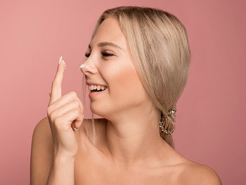 Eine lächelnde junge Frau trägt eine Creme auf ihre Nase auf