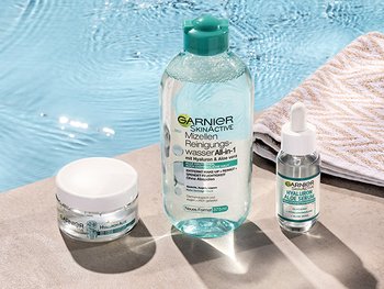 Gesichtscreme, Mizellenwasser und Serum gegen Unreinheiten am Rand eines Pools neben einem Handtuch