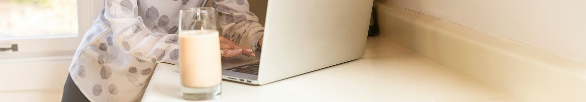 Jemand arbeitet an einem Laptop und daneben steht ein Glas Milch