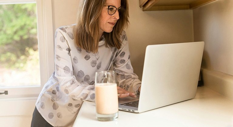Eine Frau arbeitet am Laptop daneben steht ein Glas Milch