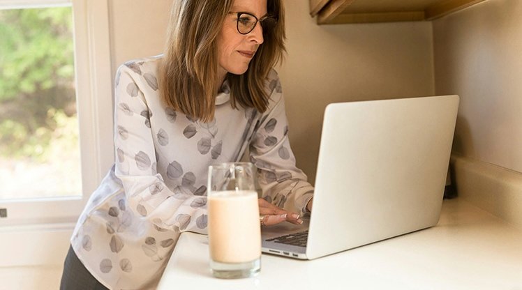 Eine Frau arbeitet am Laptop daneben steht ein Glas Milch