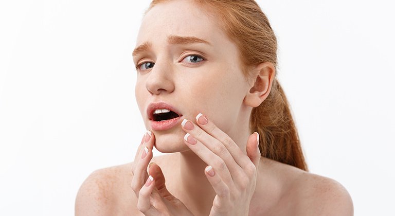 Eine junge Frau schaut erschrocken und fasst sich mit beiden Händen an ihren Kinnbereich