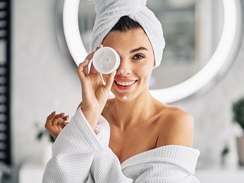 Frau, die sich eine Gesichtscreme vor ihr Auge hält