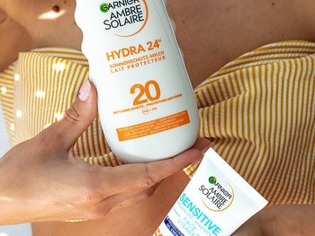 Hände einer Frau, die wie Garnier Sonnenschutzprodukte vor ihr gelbes Bini-Oberteil hält