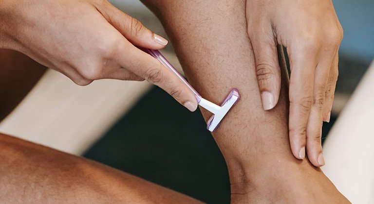 Eine Frau rasiert sich die Wade mit einer Einwegrasierer