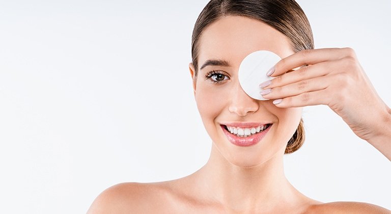 Junge Frau hält sich ein Reinigungspad vor ihr linkes Auge