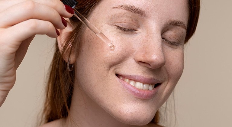 Gesicht einer Frau mit Sommersprossen, die sich ein Serum aufs Gesicht gibt