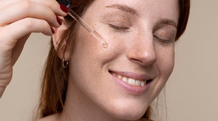 Gesicht einer Frau mit Sommersprossen, die sich ein Serum aufs Gesicht gibt