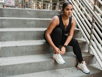 Eine junge Frau bindet sich die Sportschuhe zu, sitzend auf einer Treppenstufe