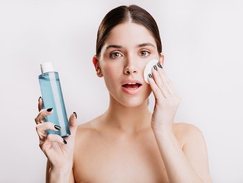 Frau die einen Gesichtsreiniger in der Hand hält und sich das Gesicht mit einem Wattepad abschminkt