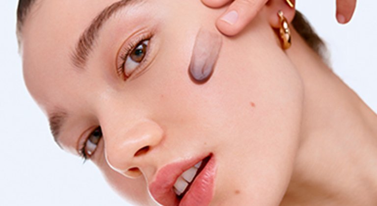 Eine junge Frau trägt ein Gesichts-Peeling auf ihre linke Wange auf