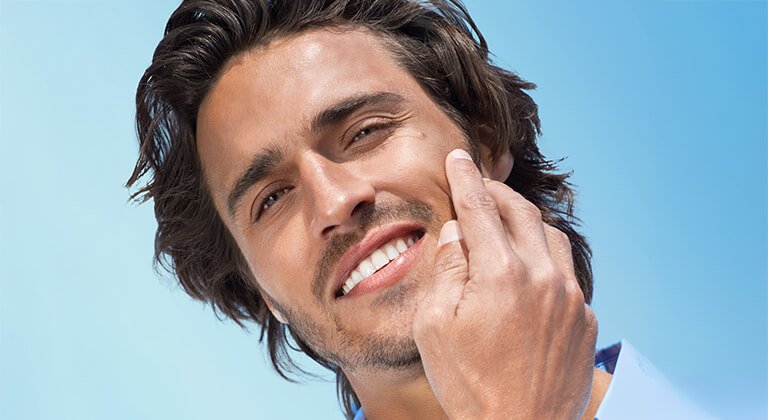 Lächelnder Mann streicht mit der Hand über seine Wange