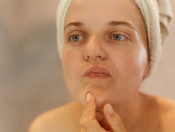 Eine Frau betrachtet ihre Haut im Spiegel