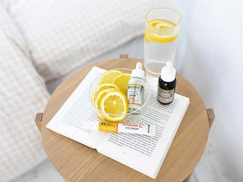 Nachttisch mit Zitronenscheiben, Vitamin C Augencreme sowie Tag- und Nachtserum von Garnier auf einem Buch