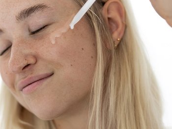 Junge Frau träufelt mit einer Pipette Vitamin-C-Serum auf ihre Wange