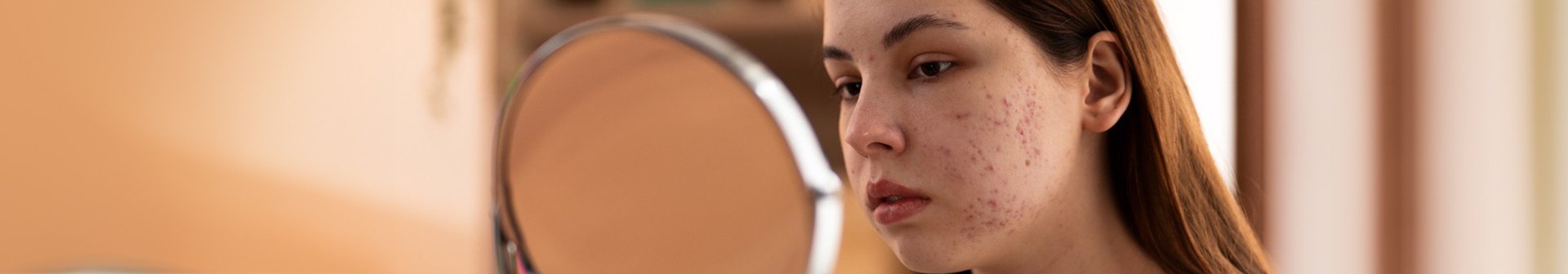 Eine junge Frau betrachtet ihr Gesicht in einem runden Spiegel