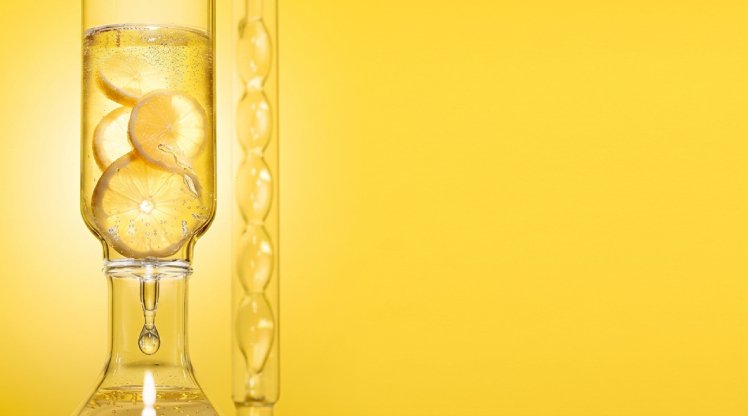Visualisierung von Vitamin C für Anti-Aging, Zitronen in einem Behältnis aus Glas vor gelbem Hintergrund